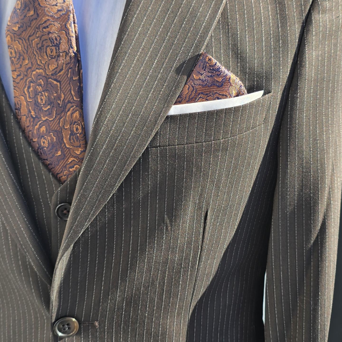 Close-up photograph of a dark pinstripe suit jacket with a patterned tie and folded pocket square, brightly lit indoors.
