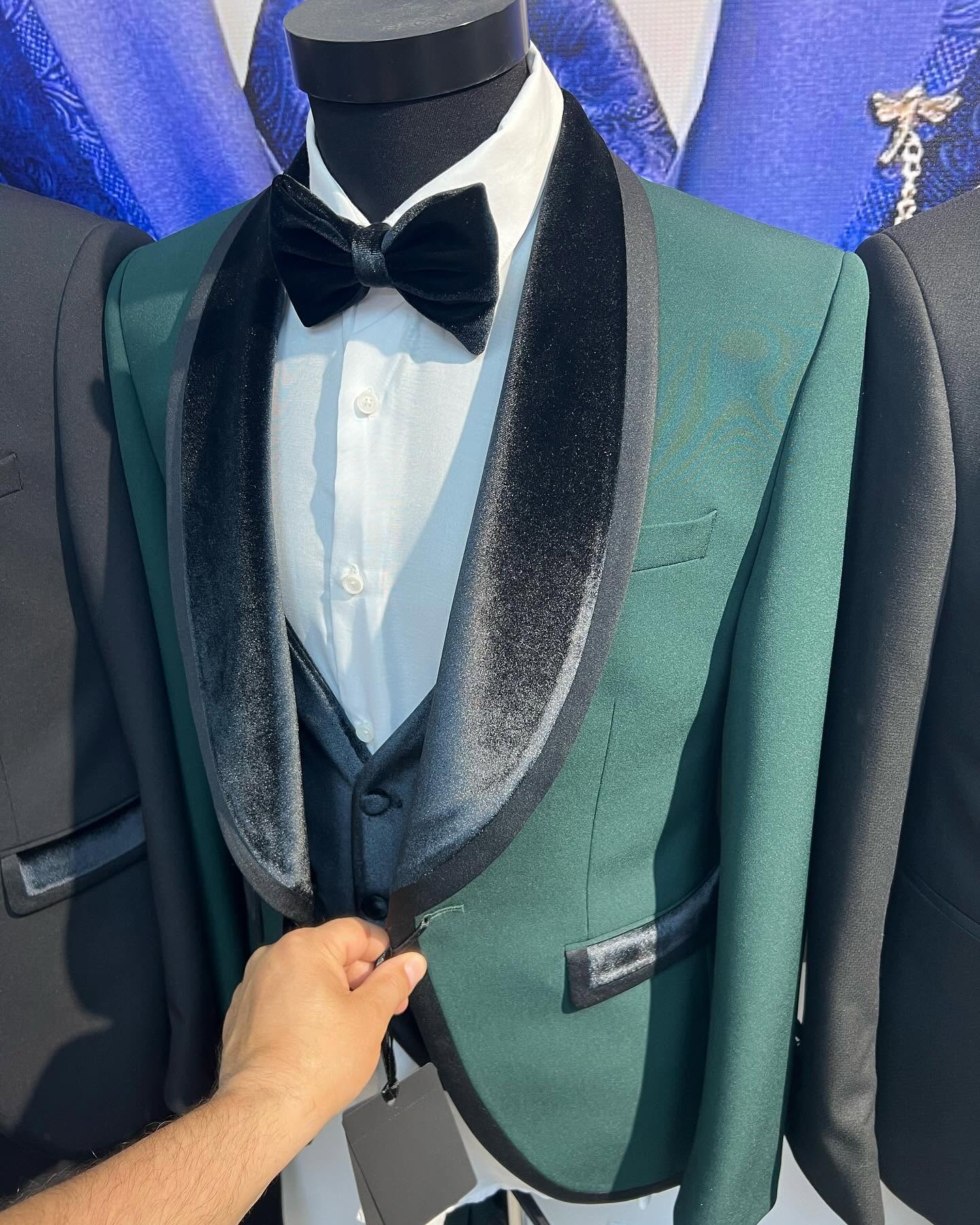 Close-up of a green tuxedo jacket and bow tie on a mannequin, with a hand adjusting the front, brightly lit.